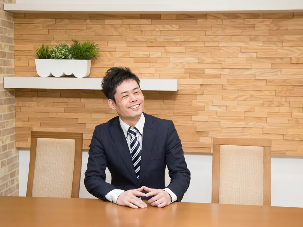 スーツ姿の鑑定士が、机に両手を組んで笑顔で話している写真