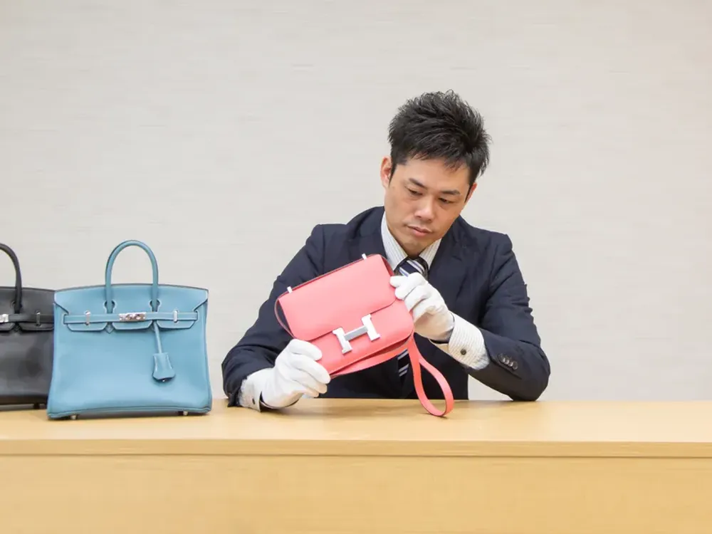 エルメスのバッグを手袋で持って確かめている写真。奥に青いバーキンが置かれている
