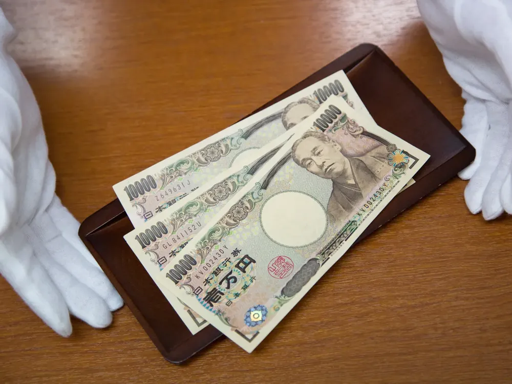 白い手袋の手と、お盆に載った1万円札3枚の写真