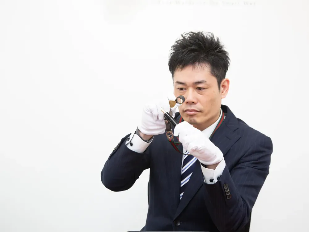 スーツ姿の鑑定士が、白い手袋でルーペを使い、品物を確かめている写真